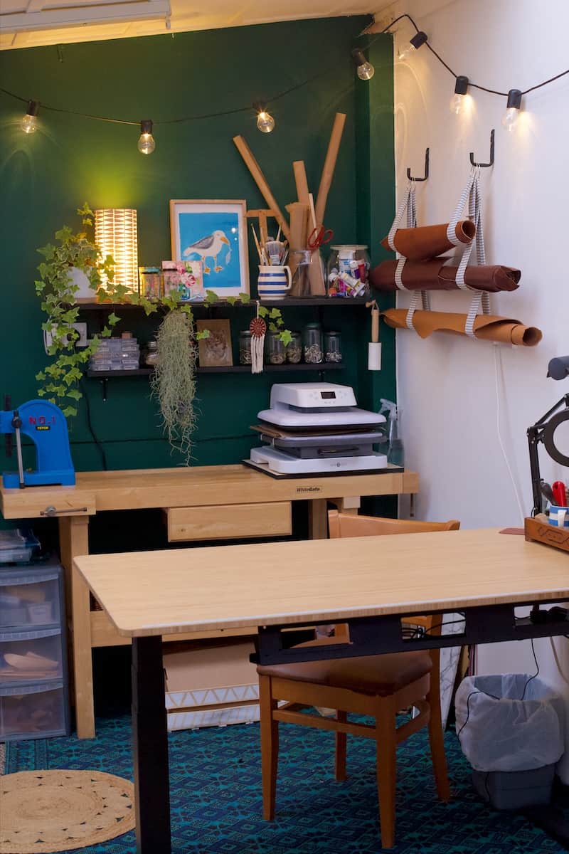 Small art and leather studio with dark green wall, pine tables, and lots of colourful paintings
