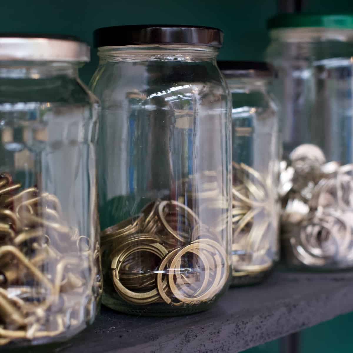 Mismatched glass jars containing keyrings and buckles for leather making