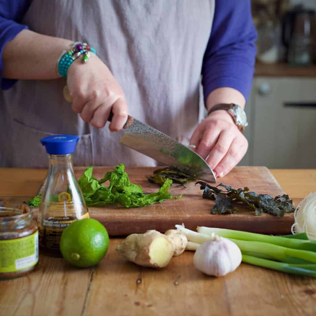 Woman in grey chopping freshly picked seaweed on a wooden board on a wooden kitchen counter